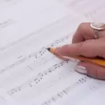 Detailed shot of a hand writing music notes on sheet music, reflecting creativity and composition.