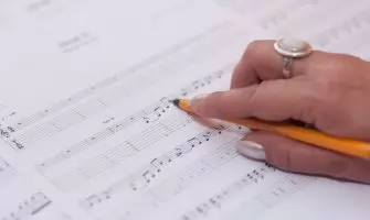 Detailed shot of a hand writing music notes on sheet music, reflecting creativity and composition.