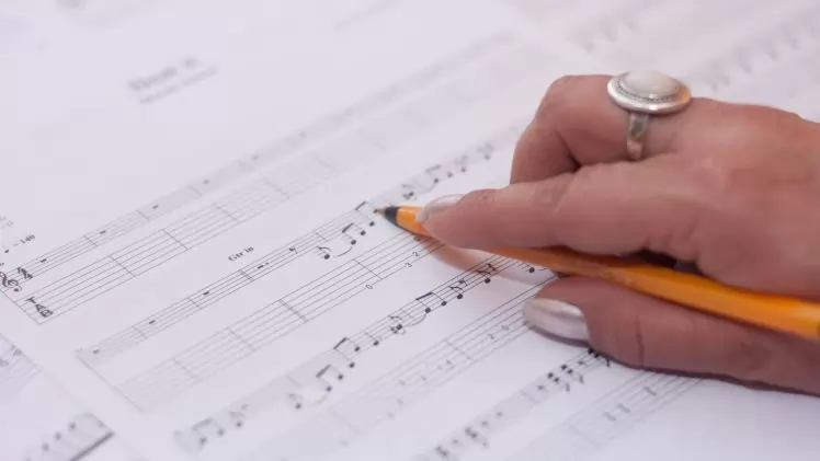 Detailed shot of a hand writing music notes on sheet music, reflecting creativity and composition.