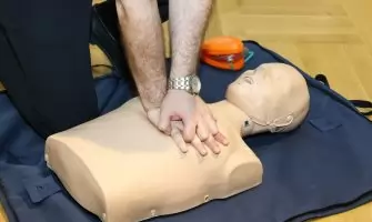 Hands performing CPR on a training dummy using realistic techniques indoors.