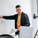 Professional instructor teaching math concepts online with a laptop and whiteboard.