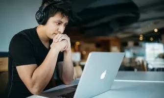 Homem Usando Fones De Ouvido Enquanto Sentado Na Cadeira Em Frente Ao Macbook 4 EeTnaC1S4