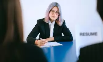 A young woman with dyed hair takes notes during a job interview.