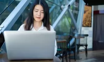 Asian woman working on a laptop in a modern cafe, exemplifying digital entrepreneurship and remote work.