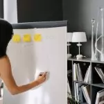 Woman planning business strategy on whiteboard in office setting, writing 100% improvement goals.