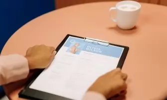 Close-up of hands holding resume during interview with coffee on table, highlighting workplace setting.