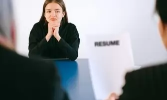 A woman in a job interview facing two employers with a focus on her resume.