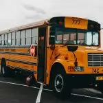 Classic American yellow school bus parked by a serene lakeside in an urban setting.