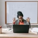 Cheerful African American female teaching online lesson with netbook in modern classroom