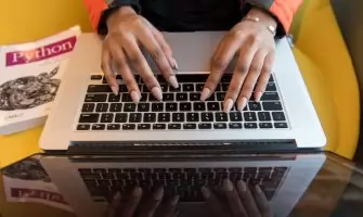 A person typing on a laptop with a Python programming book visible, capturing technology and learning.