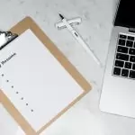 A clipboard with a resume beside a pen and laptop on a marble desk, ideal for business and job application themes.