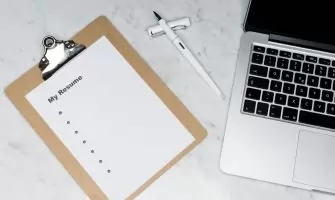 A clipboard with a resume beside a pen and laptop on a marble desk, ideal for business and job application themes.